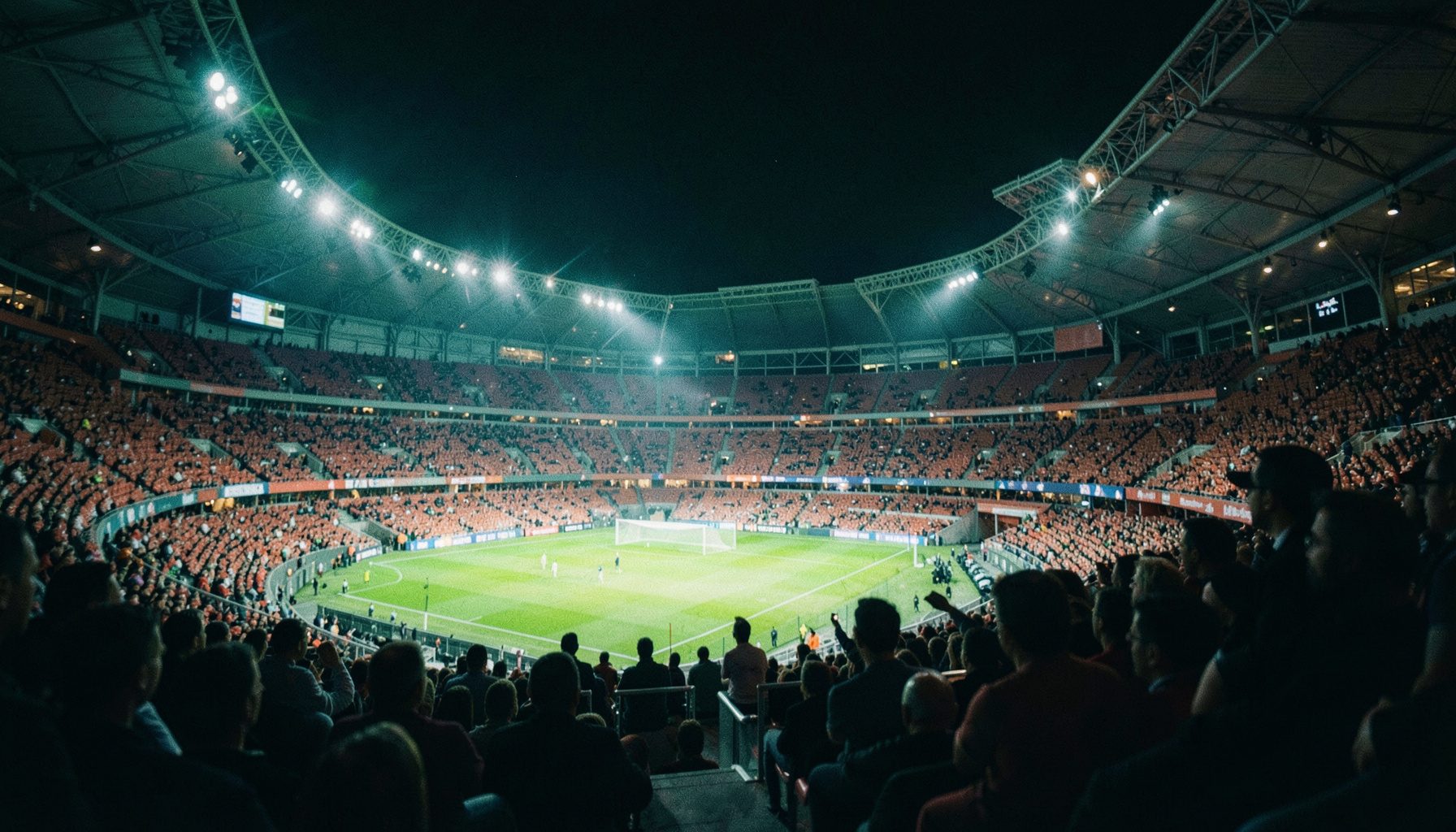 Gece aydınlatmalı modern bir futbol stadyumu, tribünlerde seyirci silüetleri, lacivert ve turuncu tonlar