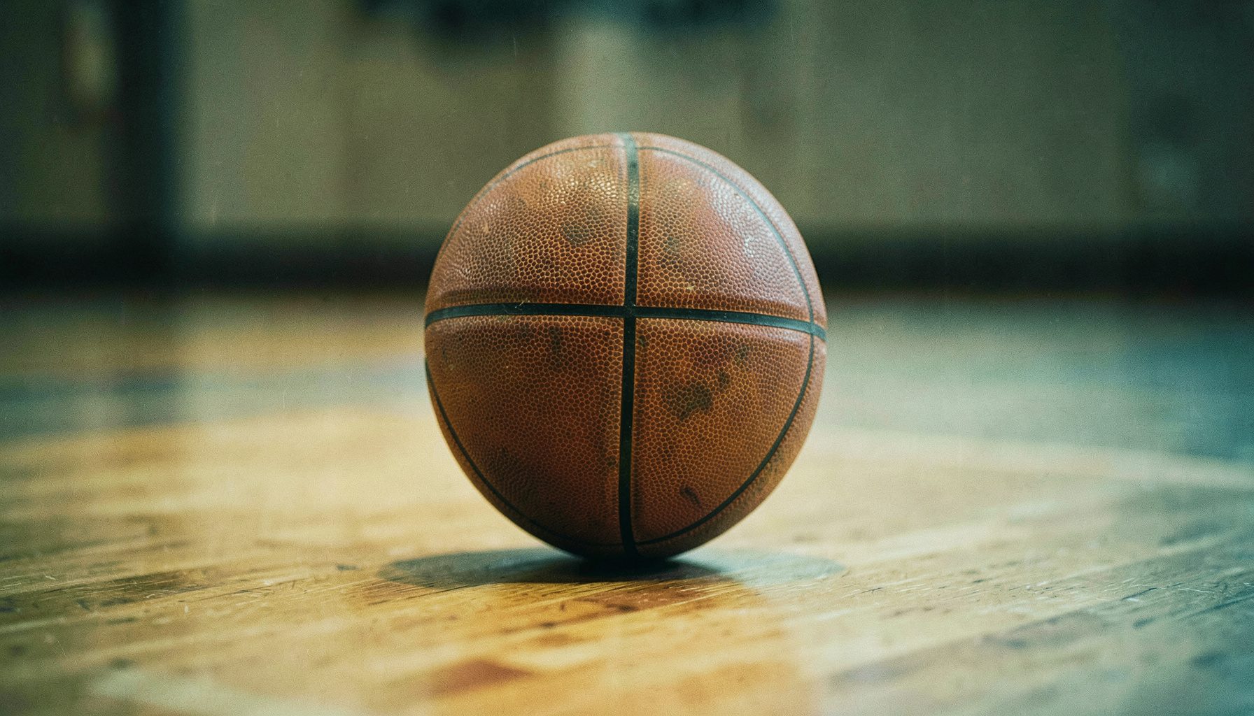 Turuncu ağırlıklı sıcak tonlarda, bir basketbol topunun parke zeminde yakın çekim görüntüsü